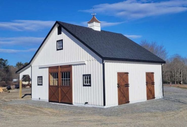 white siding large horse barn with wooden doors and a lean to