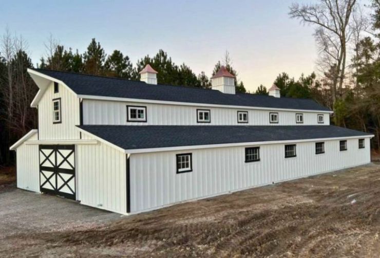 long monitor barn with white siding on a dirt ground in the evening