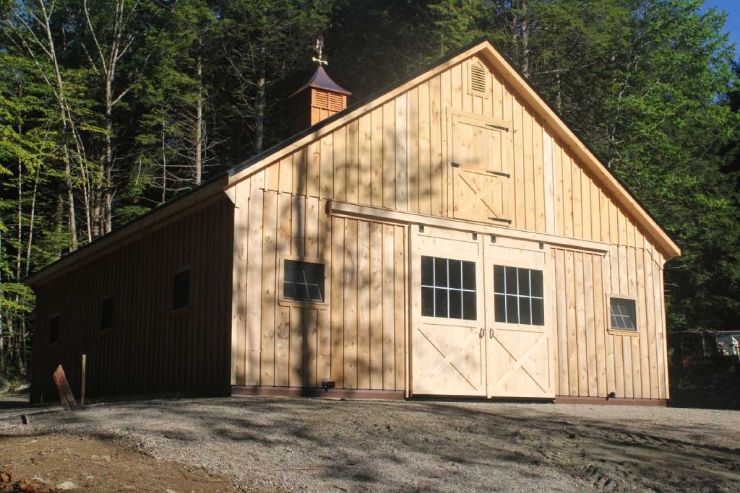 A large wooden A-Frame barn roof style with sliding doors and windows in the woods