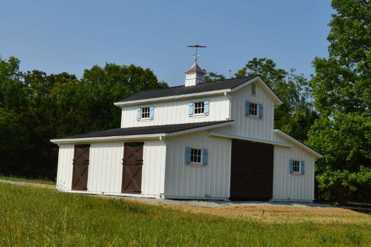 A raised center type of barn roof sitting in the middle of a field, with a weather vane on top