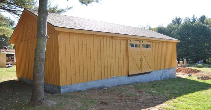 natural wood stained custom garage with sliding dutch barn doors in a field