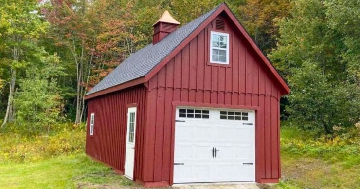 red mini garage with white garage door and side access door in front of tree line