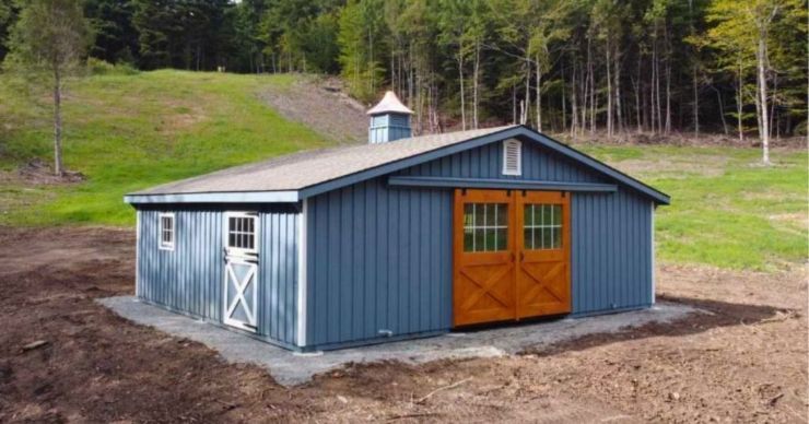 gray blue barn with wooden double doors and a side service door on a property