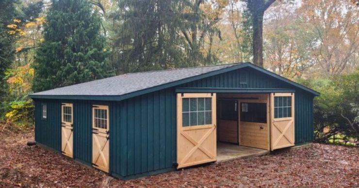 dark green horse barn with natural stained doors in the woods