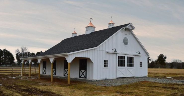 white barn with four horse barn doors with black trim under a lean to at dusk